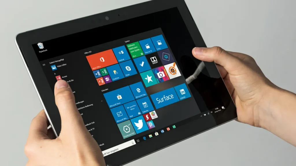 Tablet preto sendo segurado nas mãos em um ambiente moderno e bem iluminado.