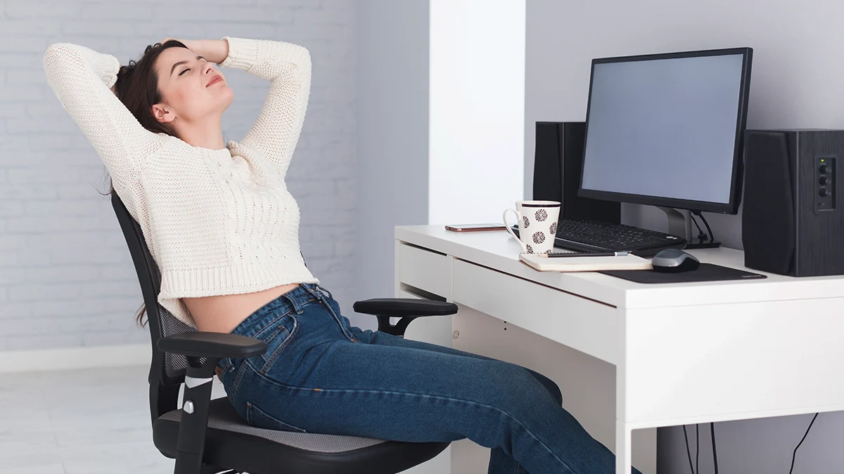 Mulher sentada relaxada em cadeira ergonômica preta em uma sala de escritório moderna.