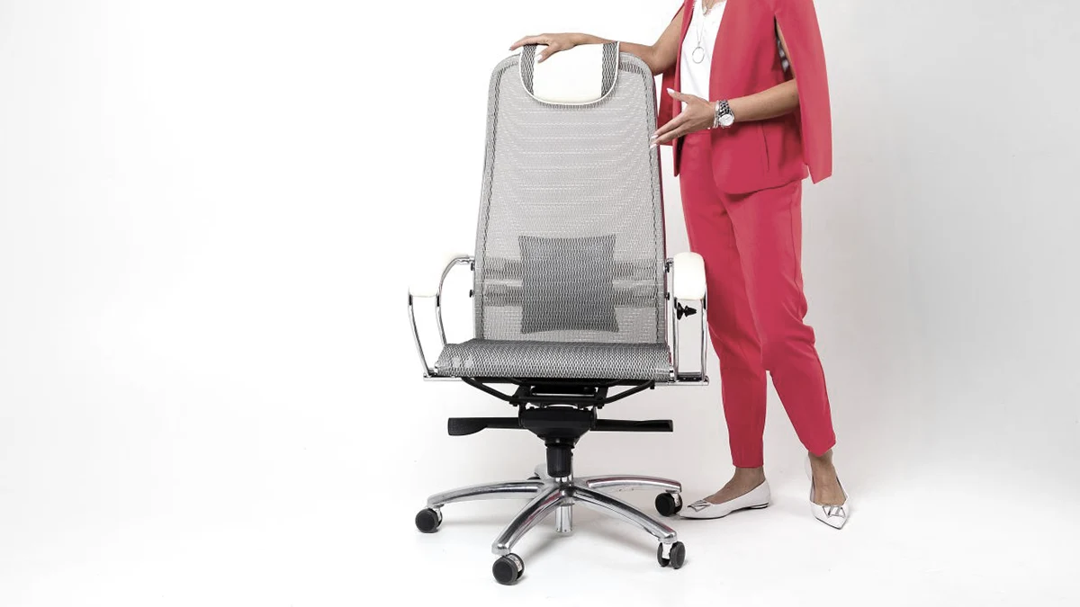 Mulher apresentando uma cadeira de escritório ergonômica cinza em uma sala moderna.