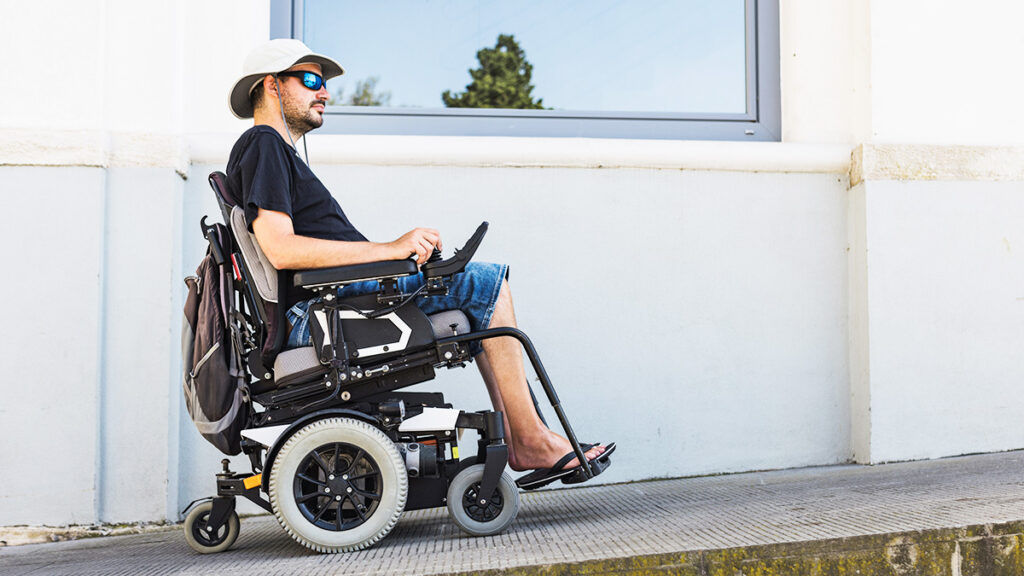 Homem utilizando uma cadeira de rodas motorizada subindo uma ladeira em um ambiente externo.